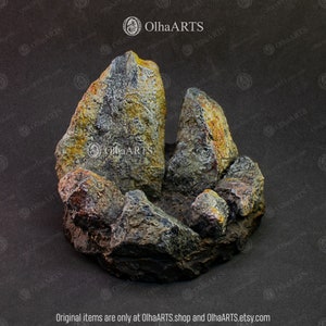 May include: A small, gray, brown, and yellow rock formation with a rough, textured surface. The rock formation is shaped like a small mountain range.