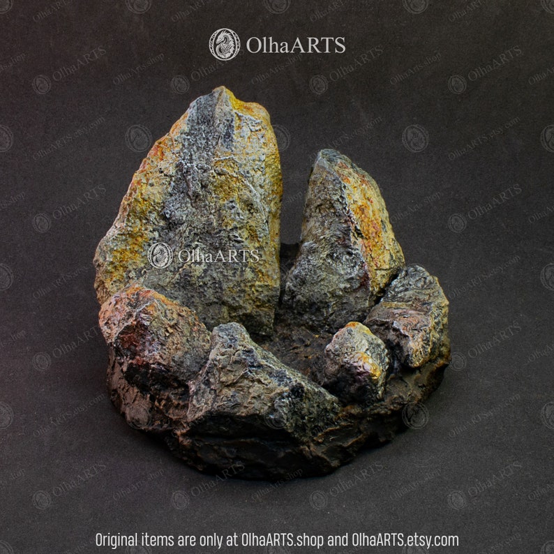 May include: A small, gray, brown, and yellow rock formation with a rough, textured surface. The rock formation is shaped like a small mountain range.