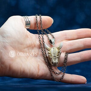 May include: A silver chain necklace with a white and brown dragon skull pendant. The pendant is detailed with teeth and horns.