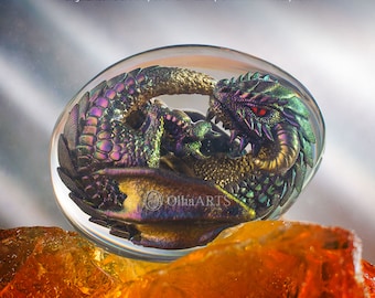 May include: A small, iridescent green and gold dragon sculpture is encased in a clear glass sphere. The dragon is curled up with its head resting on its tail. The sphere is sitting on a bed of orange and yellow crystals.
