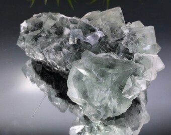 Könnte beinhalten: Ein Cluster aus grünen Fluoritkristallen mit glasartigem, durchscheinendem Aussehen. Die Kristalle sind in einer zufälligen, natürlichen Formation angeordnet.