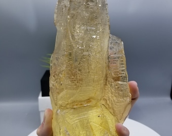 May include: A large, clear, yellow quartz crystal with a pointed tip. The crystal has a rough, textured surface and is translucent.