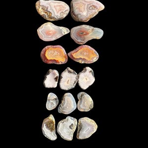 May include: A collection of 14 agate slices, each with unique patterns and colors, including white, brown, orange, and pink. The slices are arranged in a vertical stack against a black background.
