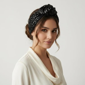 Puede incluir: Una diadema negra con lentejuelas y un diseño anudado. La diadema es ancha y cubre la frente. Las lentejuelas negras brillan. Un accesorio para el cabello elegante.