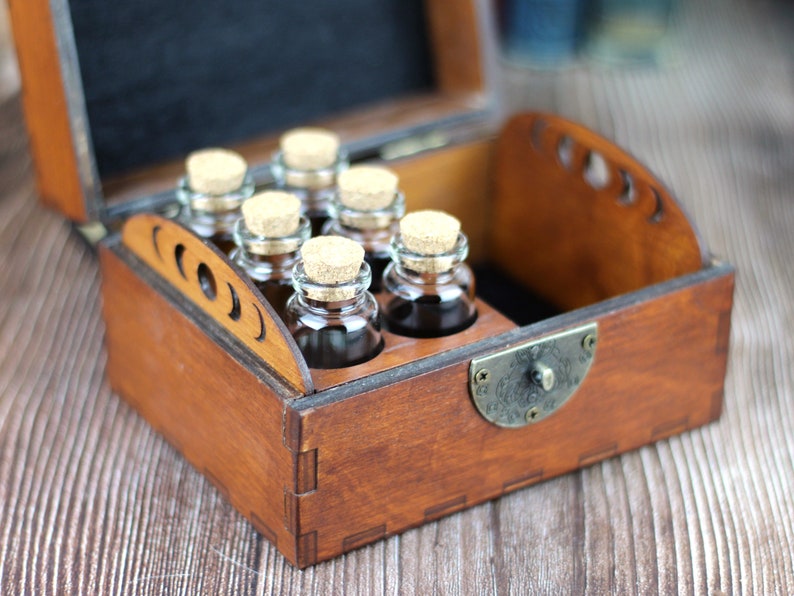 May include: A wooden box with a hinged lid, containing six small glass bottles with cork stoppers. The box is stained a warm brown color and has decorative cutouts on the side. The bottles are filled with a dark liquid.