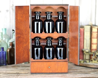 Wooden apothecary cabinet with drawer and holding six brown medicine bottles with glass stoppers