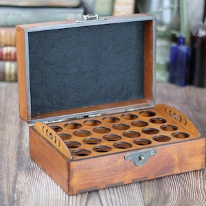 May include: Open wooden box with multiple circular compartments, ideal for storing small items. The box is stained a warm brown color, with a black felt interior and a metal clasp. The lid is open, revealing the interior.