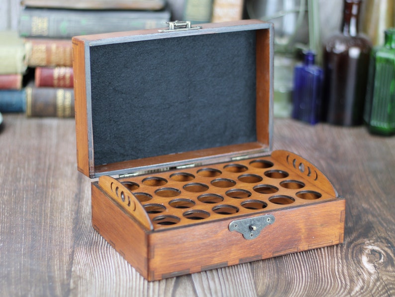 May include: Open wooden box with multiple circular compartments, ideal for storing small items. The box is stained a warm brown color, with a black felt interior and a metal clasp. The lid is open, revealing the interior.