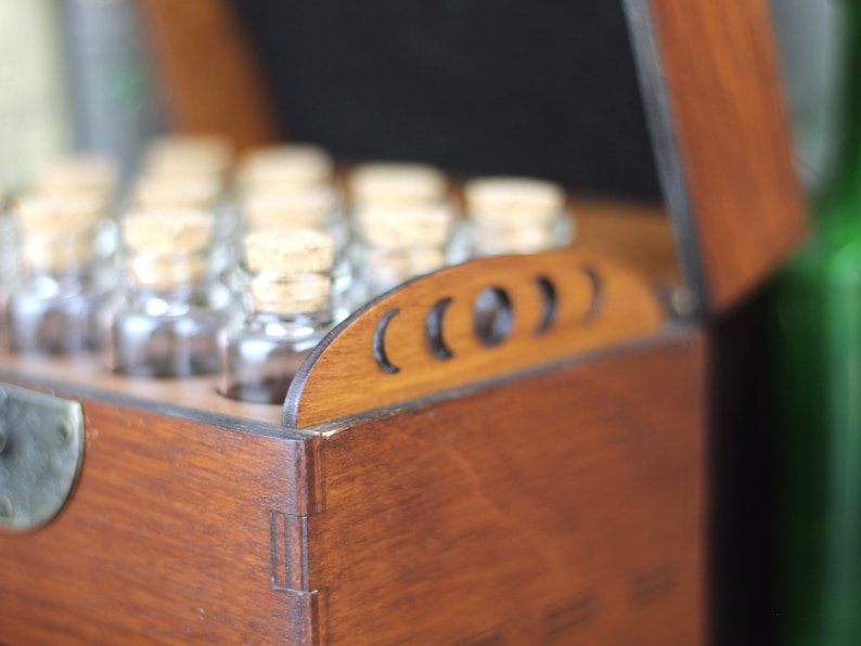 May include: A wooden box with a hinged lid, filled with small glass bottles, each sealed with a cork stopper. The box is stained a warm brown color, and the lid features decorative cutouts. The bottles are arranged neatly inside.