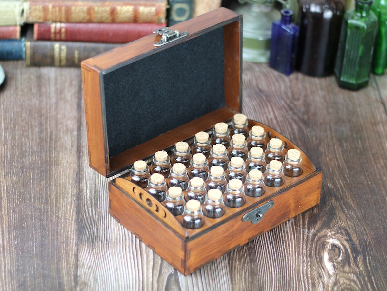May include: A wooden box with a hinged lid, containing small glass bottles with cork stoppers. The box is stained a warm brown color and has a black felt lining. The bottles are arranged in rows.