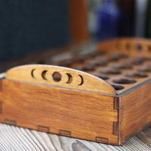 May include: A wooden box with a dark stain, featuring a crescent moon design on the top edge. The box is open, revealing multiple circular compartments inside. A metal clasp secures the lid. The box is likely for storing small items.