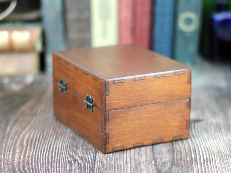 May include: A rectangular wooden box with a hinged lid and metal clasp closures. The box is stained a warm brown color and features visible joinery details. The box is sitting on a wooden surface.