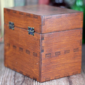 May include: A stained wooden box with a hinged lid and metal clasp. The box is a warm brown color and features decorative joinery details. The box is a cube shape and appears to be empty.