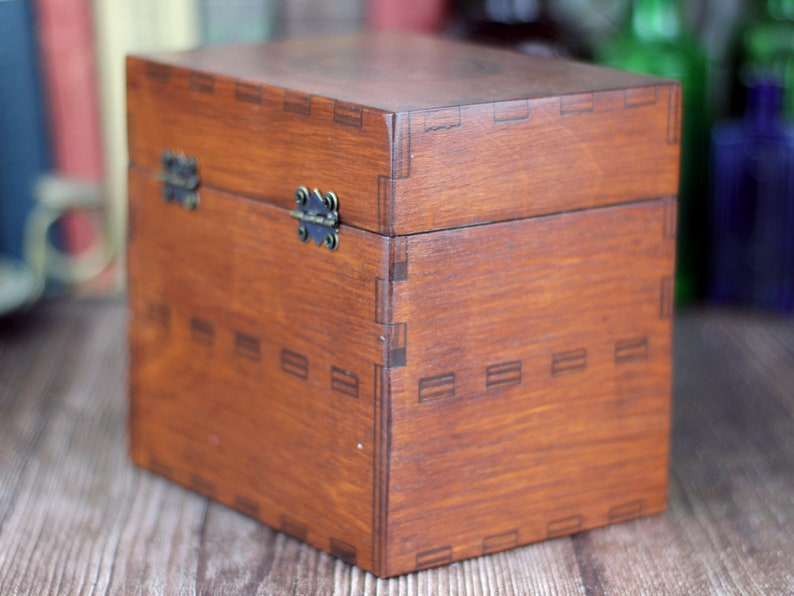 May include: A stained wooden box with a hinged lid and metal clasp. The box is a warm brown color and features decorative joinery details. The box is a cube shape and appears to be empty.