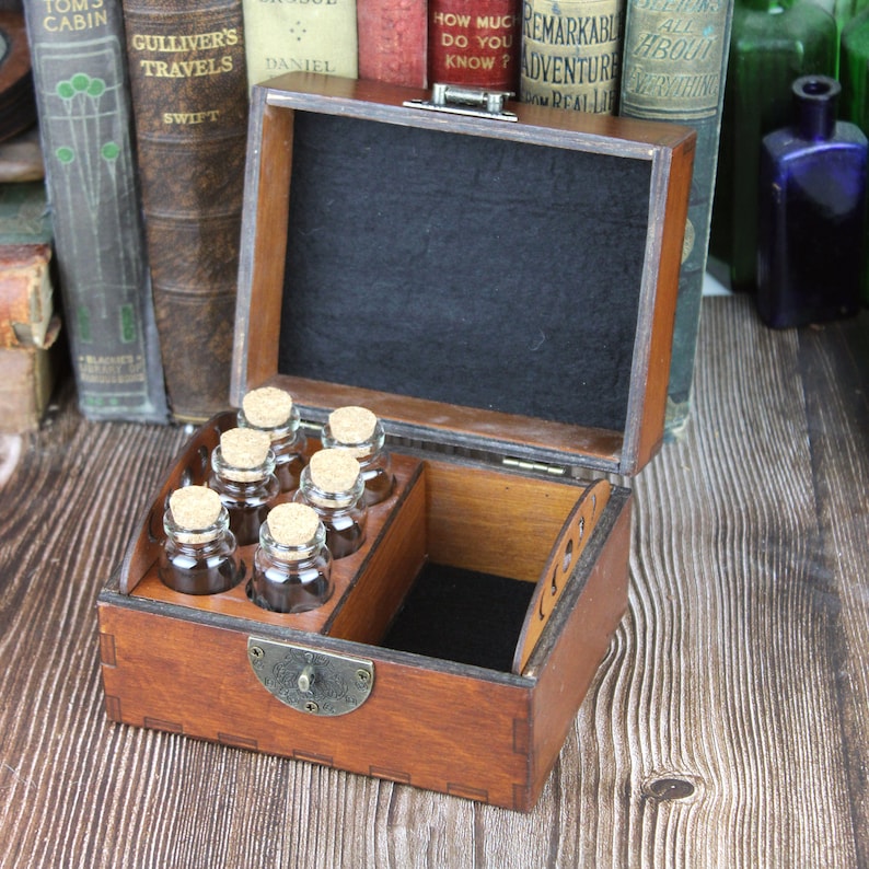 May include: A wooden box with a hinged lid, open to reveal small glass bottles with cork stoppers. The box is stained a warm brown and lined with black fabric. The bottles are arranged in a tray.