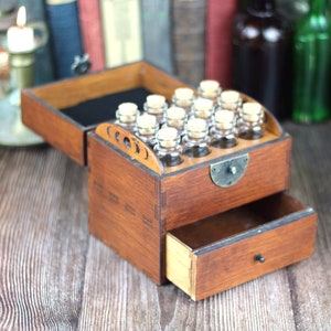 May include: A wooden apothecary chest with a drawer and a hinged lid. The lid is open, revealing small glass bottles with cork stoppers. The chest is stained a warm brown color and has decorative cutouts on the front.