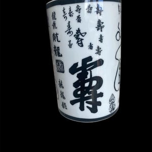 May include: White ceramic tumbler with black calligraphy and illustrations. The tumbler features a black rim and base, with various Chinese characters and symbols decorating the surface. The design is a mix of vertical and horizontal text, creating a visually interesting pattern.