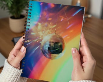 Op de afbeelding: Spiraalgebonden notitieboek met een kleurrijke regenboogachtergrond en een hangende discobal. Het omslagontwerp heeft een retro feestthema, met een zilverkleurige discobal tegen een levendige achtergrond.