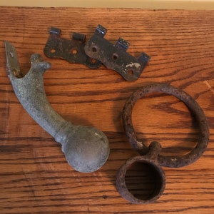 May include: A collection of four rusty metal hardware pieces, including two hinges, a ring, and a decorative handle with a ball finial.