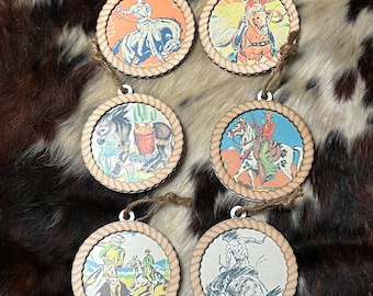 Puede incluir: Seis adornos redondos de madera con ribete de cuerda, cada uno con una ilustración vintage de un vaquero montando un caballo o un burro. Las ilustraciones son coloridas y presentan una variedad de escenas, incluyendo un vaquero montando un caballo a través de un paisaje desértico, un vaquero montando un burro con un cubo de naranjas y un vaquero montando un caballo con una pistola.