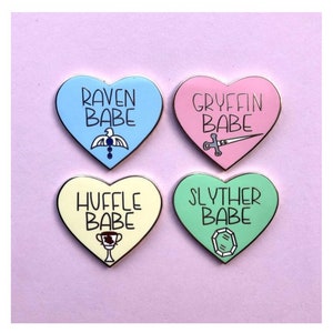 May include: Four heart-shaped enamel pins with different Hogwarts house colors and crests. The pins say "Raven Babe", "Gryffin Babe", "Huffle Babe", and "Slyther Babe".