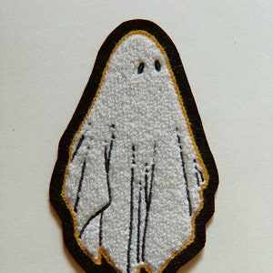 May include: White felt ghost patch with black embroidered eyes and a black outline with a yellow accent.