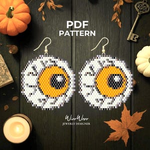 Puede incluir: Un par de pendientes redondos de cuentas con un diseño gráfico de globo ocular que presenta un iris naranja brillante, una pupila negra con un reflejo blanco y una esclerótica blanca con venas grises. El texto PDF PATTERN es visible.
