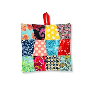 May include: A colorful patchwork pot holder with a red hanging loop. The pot holder is made of various fabrics in shades of blue, green, red, pink, yellow, and black.