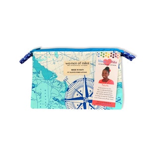 May include: A blue and white map print zippered pouch with a compass design. The pouch is made in Haiti by talented women artisans. The tag attached to the pouch reads "Women of Milot Entrepreneurial Network" and features a portrait of a woman named Felicita. The text on the tag reads "Felicita loves to sew. She is a talented artisan and a true success story. She and her husband have a young son and are building a new home in La Petite Anse. Visit us on Facebook or at womenofmilot.com."
