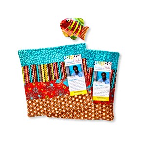 May include: Two colorful fabric pouches with a variety of patterns, including teal polka dots, stripes, and floral designs. A decorative fish is above the pouches. Each pouch has a tag with a photo and text.