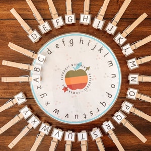 Puede incluir: Un gr&aacute;fico de aprendizaje del alfabeto colorido con un gr&aacute;fico de manzana roja y las palabras "Min&uacute;scula" y "May&uacute;scula" impresas en &eacute;l. Pinzas de madera con las letras del alfabeto est&aacute;n unidas al gr&aacute;fico.