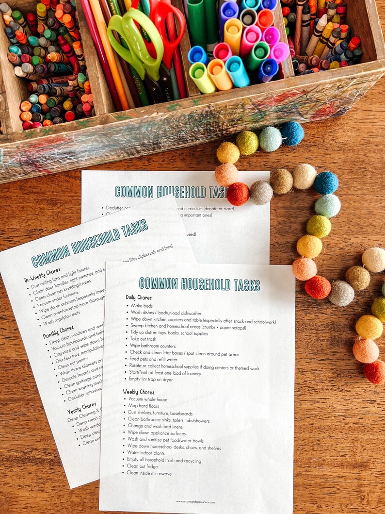 May include: Two printable checklists for common household tasks, with categories for daily, weekly, and monthly chores. The checklists are printed on white paper and are lying on a wooden table with a colorful string of beads.