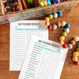 May include: A printable daily cleaning checklist with a colorful broom icon. The checklist is divided into two sections: "DOOM" and "2000: Kitchen/Laundry Room". Each section has a list of tasks with checkboxes for each day of the week.