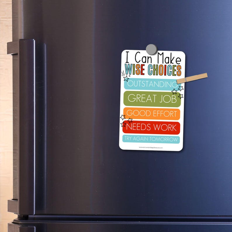 May include: A white rectangular magnet with the text "I Can Make WISE CHOICES" in colorful lettering. Below are the phrases "OUTSTANDING", "GREAT JOB", "GOOD EFFORT", "NEEDS WORK", and "TRY AGAIN TOMORROW". The magnet is attached to a black refrigerator.
