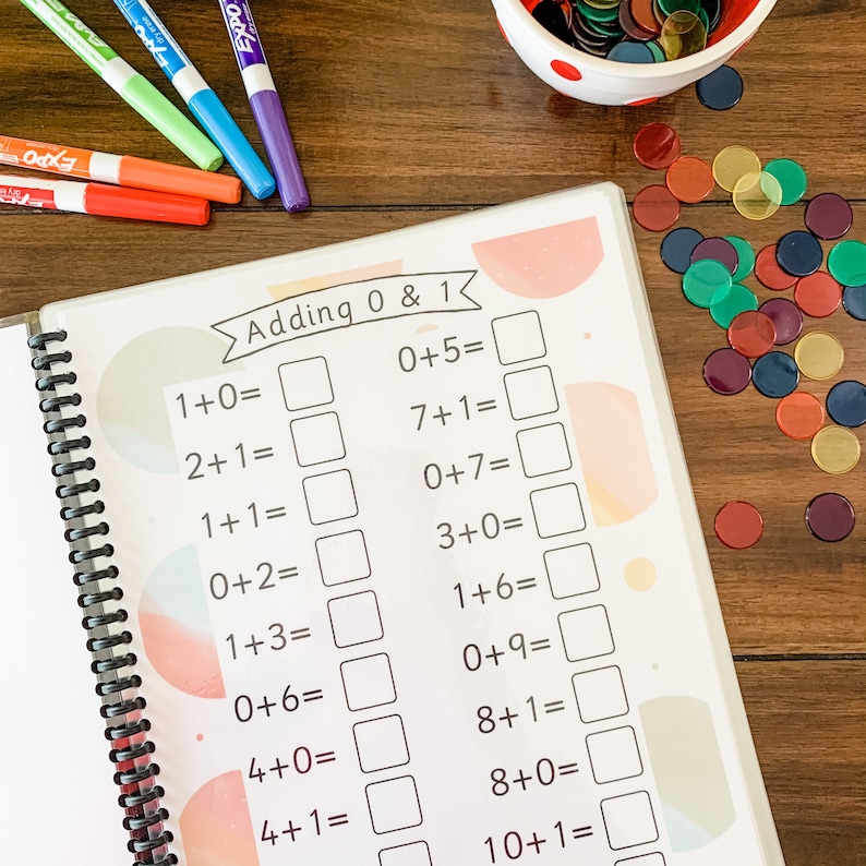 May include: A workbook with a pink and blue cover titled "Adding 0 & 1". The workbook has a spiral binding and contains math problems for children to solve. The problems involve adding 0 and 1 to various numbers.