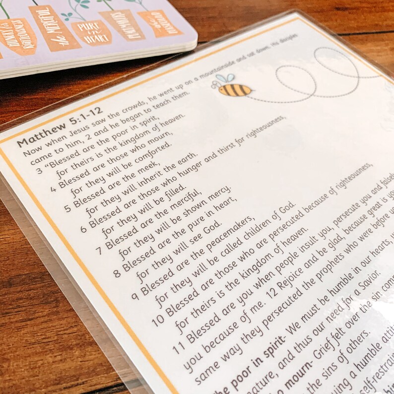 May include: A white card with a yellow bee illustration and a passage from the Bible, Matthew 5:1-12, printed in black text. The text includes the Beatitudes, a series of blessings given by Jesus in the Sermon on the Mount.