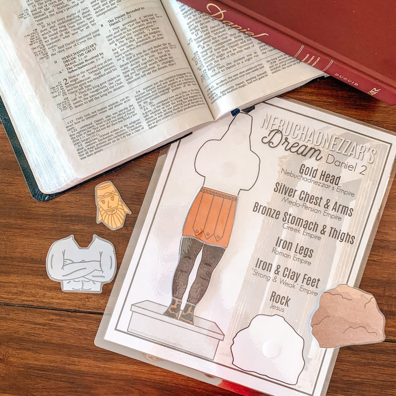 May include: A printable paper craft activity for kids featuring a paper doll representing Nebuchadnezzar's dream from the Bible. The dream is depicted as a large statue with different colored sections representing different empires. The statue has a gold head, silver chest and arms, bronze stomach and thighs, iron legs, and iron and clay feet. The statue is standing on a platform with a rock at the bottom. The text "Nebuchadnezzar's Dream Daniel 2" is at the top of the page.