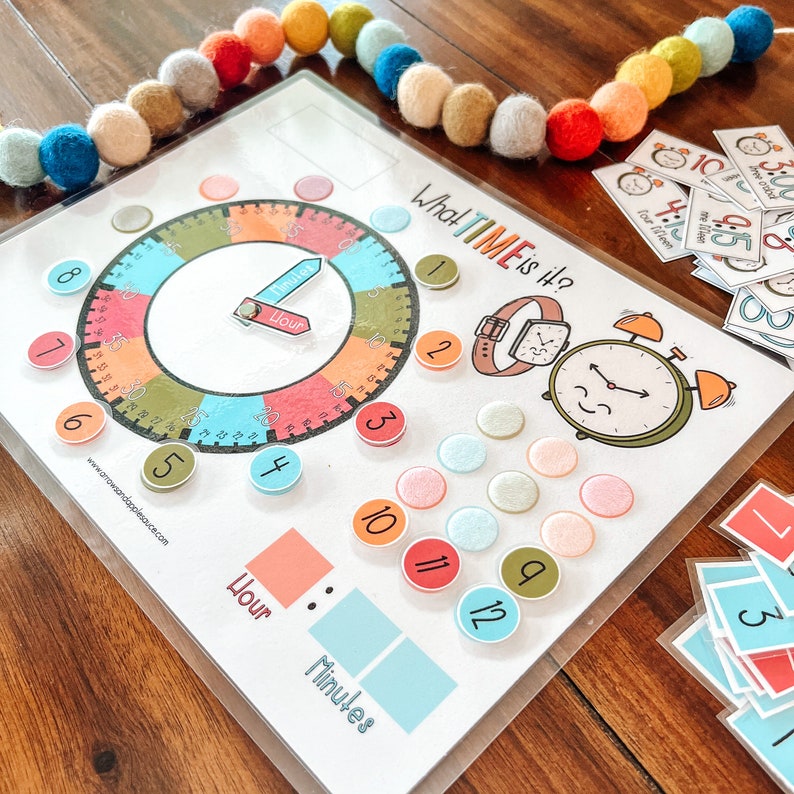 Peut inclure: Un cadran d'horloge color&eacute; avec une aiguille des heures et une aiguille des minutes mobiles. Le cadran de l'horloge est entour&eacute; de cercles color&eacute;s avec les chiffres de 1 &agrave; 12. Le cadran de l'horloge est intitul&eacute; "What TIME is it?" et comporte une petite montre et un r&eacute;veil avec un visage souriant. Il y a aussi des cercles color&eacute;s avec les chiffres de 1 &agrave; 12 autour du cadran de l'horloge.