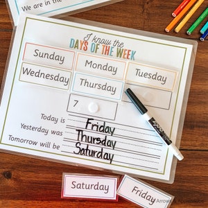 K&ouml;nnte beinhalten: Ein wei&szlig;er laminierter Lernplan mit dem Titel "Ich kenne die Tage der Woche". Der Plan hat sieben leere Felder f&uuml;r die Wochentage, wobei die W&ouml;rter "Sonntag", "Montag", "Dienstag", "Mittwoch", "Donnerstag", "Freitag" und "Samstag" in bunten K&auml;stchen darunter geschrieben sind. Der Plan enth&auml;lt auch die S&auml;tze "Heute ist", "Gestern war" und "Morgen wird sein" mit leeren Zeilen zum Eintragen der Wochentage. In der oberen rechten Ecke des Plans steht die Zahl "7". Ein schwarzer Trockenl&ouml;schmarker liegt auf dem Plan.
