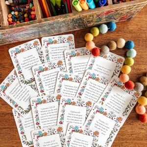 May include: A set of colorful cards with inspirational quotes and bible verses. The cards feature floral illustrations and are arranged on a wooden surface.