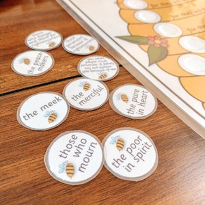 May include: A set of nine round, clear stickers with white text and a small bee illustration. The stickers feature phrases from the Beatitudes, including "the meek", "the merciful", "the pure in heart", and "those who mourn".