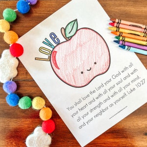 May include: A printable coloring page featuring a red apple with a smiling face and the word "Love" written above it. The page also includes a Bible verse: "You shall love the Lord your God with all your heart and with all your soul and with all your strength and with all your mind, and your neighbor as yourself. Luke 10:27"