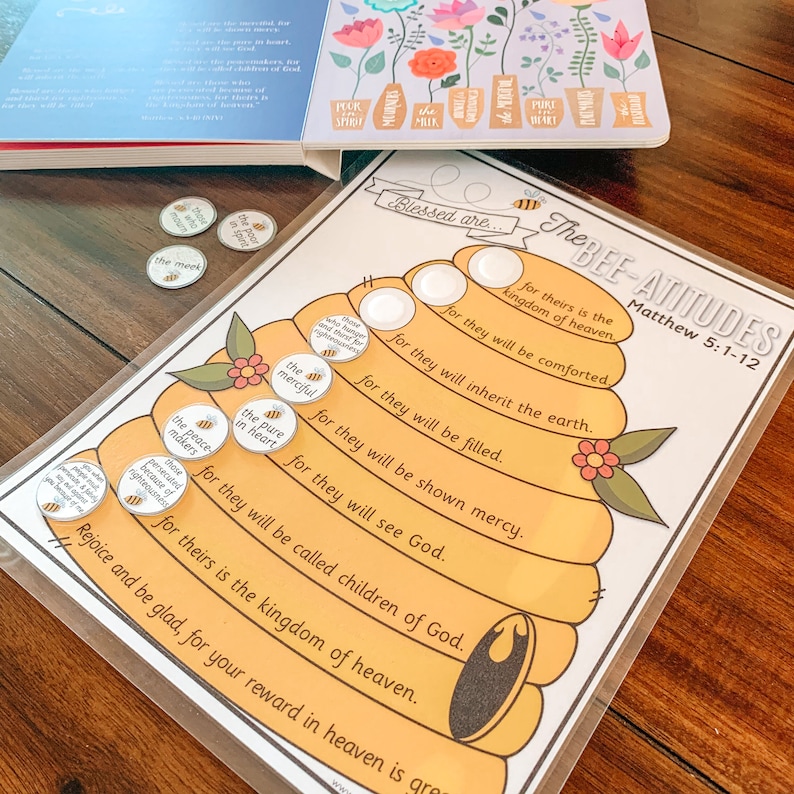 May include: A printable beehive-shaped chart with the text "The Bee-Attitudes" and "Matthew 5:1-12". The chart has eight honeycomb-shaped sections with the text "Blessed are..." and the Beatitudes from the Bible. Each section has a blank circle for a bee token. There are eight bee tokens with the Beatitudes written on them.
