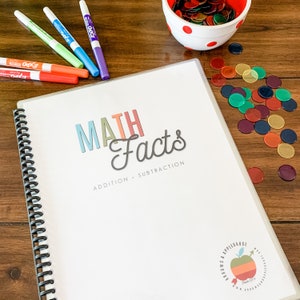 May include: A white spiral bound notebook with the text "MATH Facts" in colorful letters and the words "ADDITION - SUBTRACTION" below. The notebook has a colorful apple logo on the bottom right corner.