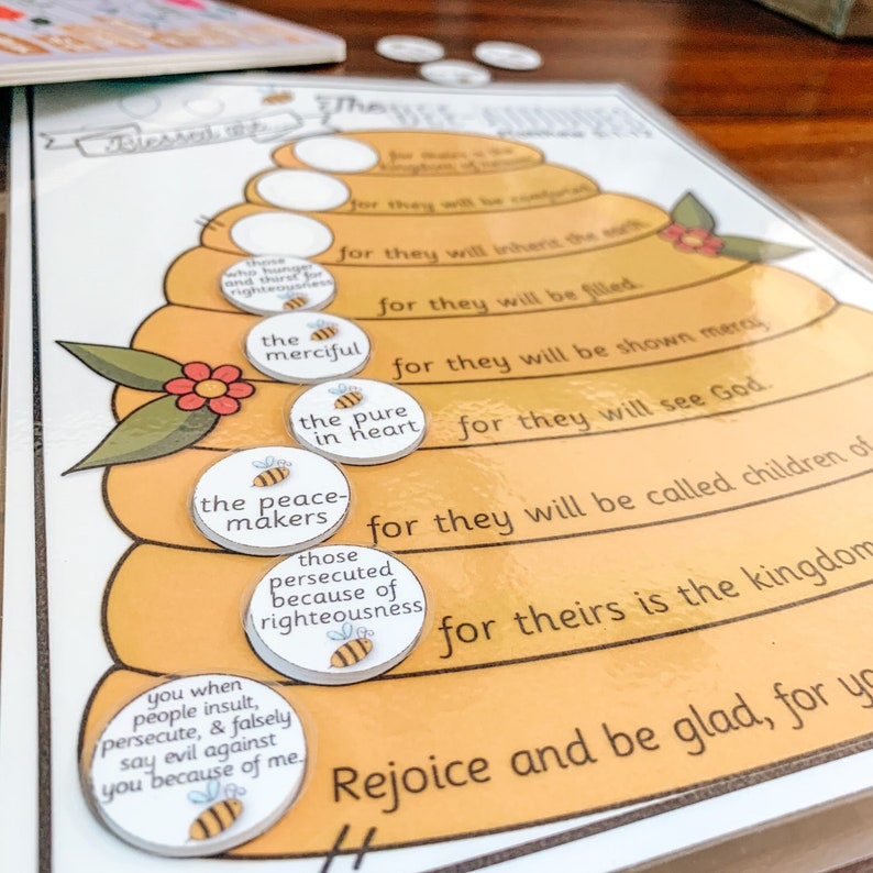 May include: A yellow and white beehive-shaped chart with the text "Blessed are the peacemakers, for they will be called children of God."  The chart has several circles with different phrases, including "the merciful", "the pure in heart", "the peacemakers", and "those persecuted because of righteousness".