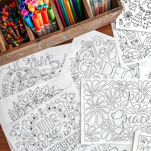 May include: A wooden box filled with colorful crayons and markers sits next to several white coloring pages. The pages feature intricate black line art designs with floral and inspirational text, ready for coloring.