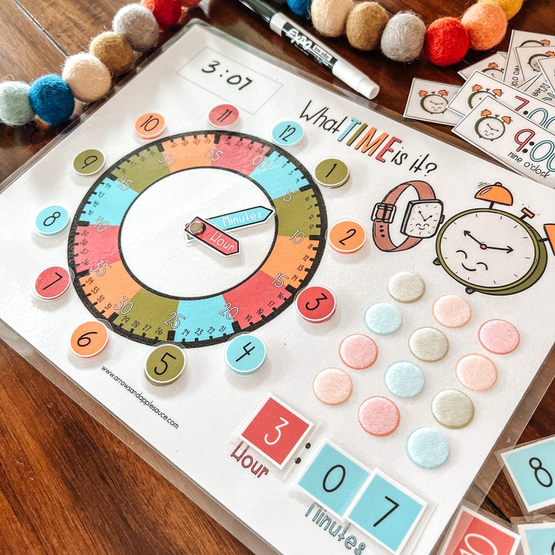 Peut inclure: Un cadran d'horloge color&eacute; avec des aiguilles mobiles et des chiffres pour apprendre l'heure. Le cadran d'horloge est entour&eacute; de cercles color&eacute;s avec les chiffres de 1 &agrave; 12. L'image comprend &eacute;galement une montre et un r&eacute;veil.