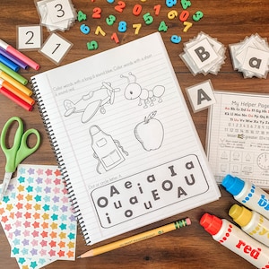 May include: A notebook with a worksheet for learning the short and long 'a' sounds. The worksheet includes a picture of an airplane, an ant, and an apple. The notebook is open to a page with the title 'Dot or circle letter A' and a chart with the letters 'A', 'e', 'i', 'o', and 'u' in different combinations.