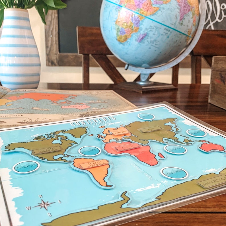 May include: A blue and green world map with continents labeled in brown. The map is on a wooden table with a globe in the background.