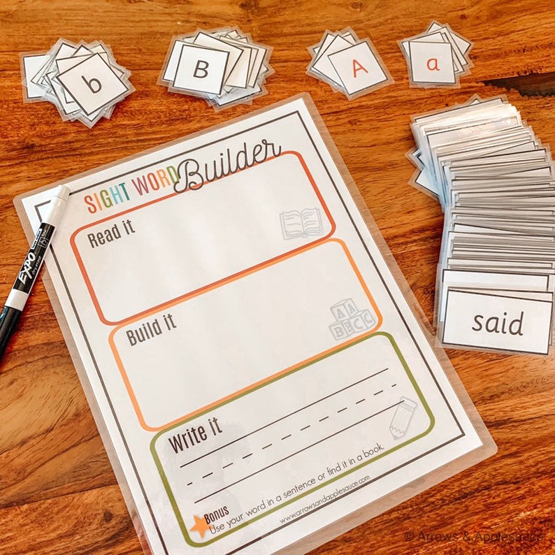 May include: A printable worksheet with the title "Sight Word Builder" and instructions to "Read it", "Build it", and "Write it". The worksheet includes a blank space for writing and a bonus section that encourages using the word in a sentence or finding it in a book. The worksheet is surrounded by a stack of flashcards with letters and sight words.